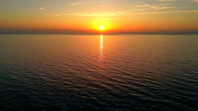Tilt up drone shot of a stunning sunset in Greece over the ocean, with birds flyng accross and a distant island on the horizon.