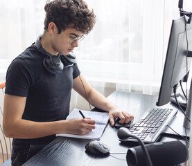 Teenager studying at home on a computer. Teen freelancer working on a project at home. Exam...