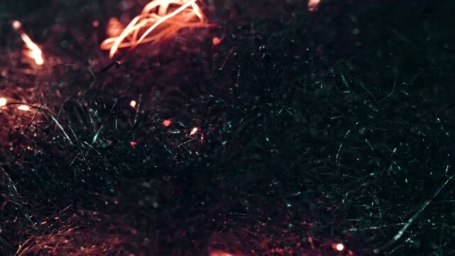 Burning embers slowly ignite dark fibrous material in a macro shot, creating a dramatic effect