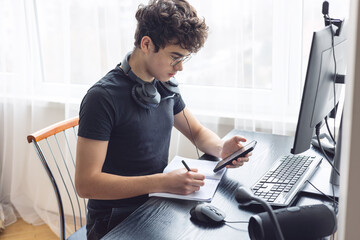 Teenager studying at home on a computer. Teen freelancer working on a project at home. Exam...