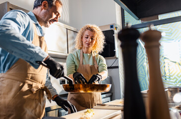 Couple enjoying a cooking class with a chef preparing meal in the kitchen.