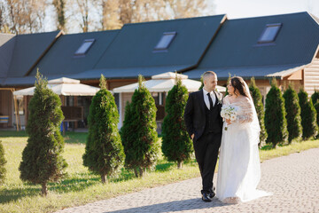 A bride and groom are walking down a path in front of a house. The bride is wearing a white dress and the groom is wearing a suit. The couple is holding hands and smiling. The house has a blue roof