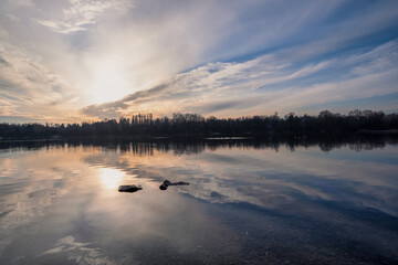 A beautifully picturesque sunset casts an array of brilliant colors over the serene and calm lake,...