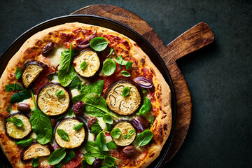 Vegetarian pizza with aubergine, spinach, tomatoes and kalamata olives. Top view. Copy space. Homemade food