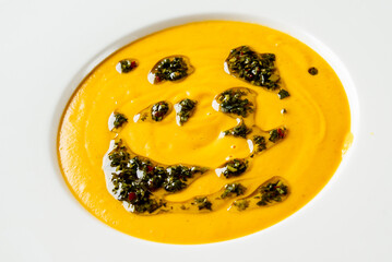 A vibrant plate featuring a smooth, creamy orange soup, artistically swirled with green herb oil. The dish combines culinary artistry with color contrast, perfect for gourmet presentations.