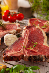Raw t bone steak, with herbs. Grill accessories. Ready for grilling. Wooden bright background.