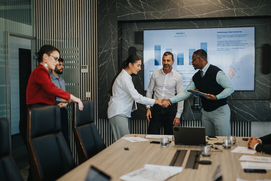 A diverse group of business people engages in a collaborative meeting. The team is discussing project details and shaking hands, showcasing teamwork and cooperation in a modern office setting.