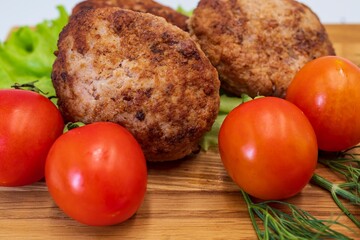 Fried chicken cutlets with vegetables on a wooden background. Meat balls with tomatoes and herbs on a wooden board.