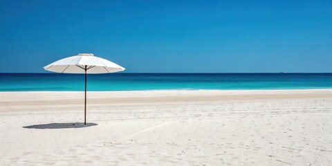 A solitary white beach umbrella casts its shadow on pristine sand, overlooking a tranquil turquoise ocean under a vibrant blue sky.