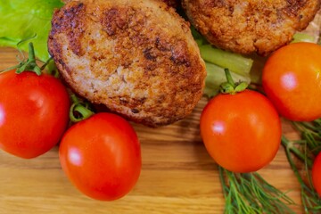 Fried chicken cutlets with vegetables on a wooden background. Meat balls with tomatoes and herbs on a wooden board.