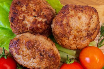 Fried chicken cutlets with vegetables on a wooden background. Meat balls with tomatoes and herbs on a wooden board.