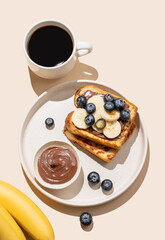 Toasted bread with chocolate cream, blueberries and banana on a plate on a beige background