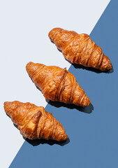 Fresh croissants lie diagonally on blue  background with shadow.