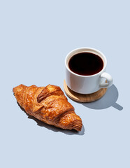  Fresh croissant and  freshly brewed espresso or americano coffee on a blue background with shadow.
