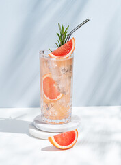 Refreshing cocktail with grapefruit, rosemary and ice in a glass on a white blue background with shadow.