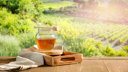 Honey in glass jar on wooden table with summer natural outdoor background. Summer time and the...
