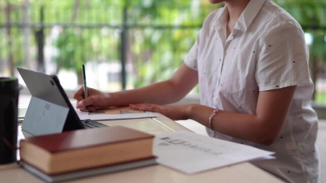 A university student studies at a table with a tablet and printed documents focusing on research in an open air study area