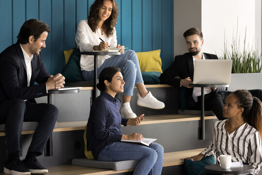 Young Indian woman make speech during group meeting, engaged in collaborative discussion in modern office room, take part at informal meeting or brainstorming session, strategy proposal, or feedback