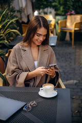 With smartphone. Beautiful young woman is outdoors of the restaurant by the table