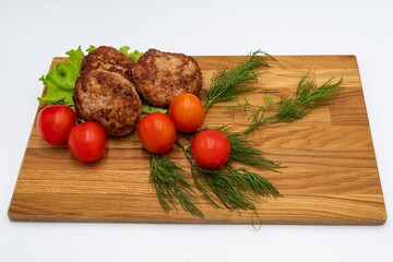 Fried chicken cutlets with tomatoes and herbs on a wooden board.