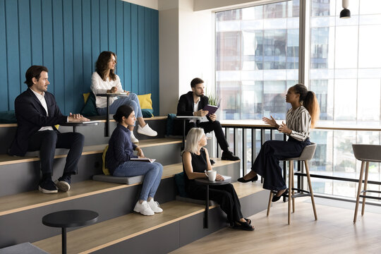 Diverse group of business people, educational seminar participants gain new knowledge, noting received information, listening attentively speech of young confident African female speaker in auditorium