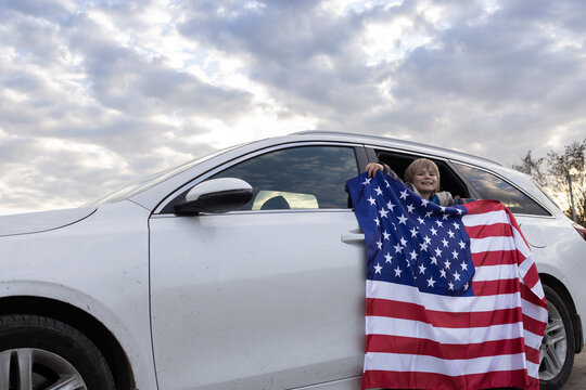white car, a child looking out of the window and holding a large American flag. Traveling by car in the United States of America. Weekend trip. Bright future