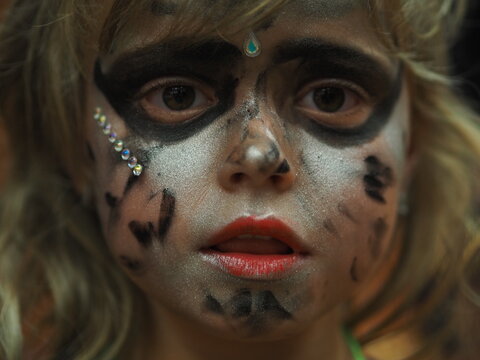 Detail of a painted face of a little girl in a witch costume at a masquerade ball