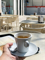 Espresso cup on a saucer with a spoon, hand holding the cup, outdoor café setting