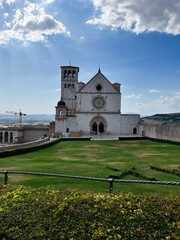 Fototapeta premium Scenic Basilica Against a Serene Landscape Under a Partly Cloudy Sky, Assisi, Italy.