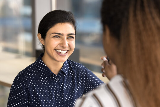 Close up cropped view attractive Indian woman employee enjoy pleasant friendly conversation with African female teammate indoors, listening ideas, creative solutions, working together on joint task