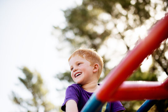 Excited, merry go round and smile with boy in forest for active play, child development or growth. Adventure, balance and game on carousel with happy kid having fun at playground in summer from below