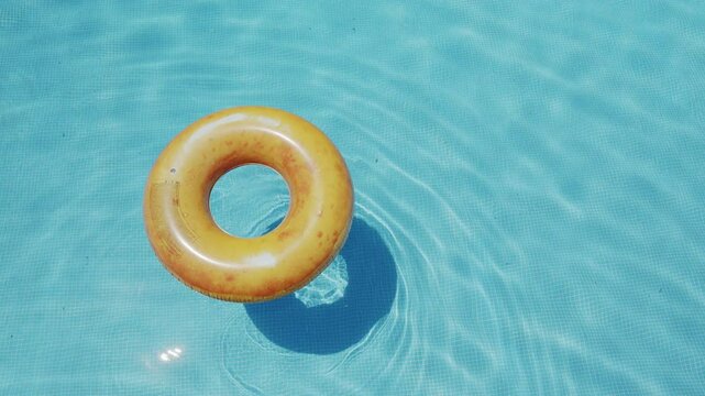 Yellow swim ring or swim tube floating over transparent water of the swimming pool. Slow motion and looped video.  