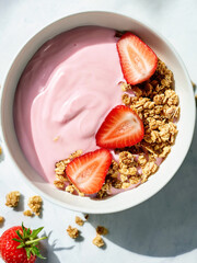 A vibrant bowl of strawberry yogurt mixed with crispy granola, presenting a visually appealing and...