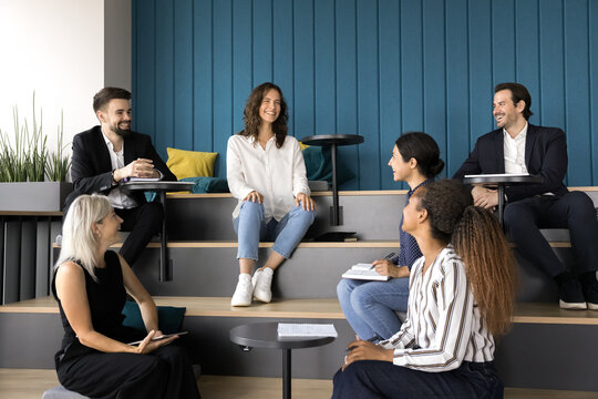Happy teammates joking and laughing during break, briefing or seminar event gathered together in modern auditorium, take part in creative workflow, opinion exchange and teamwork. Workshop, business
