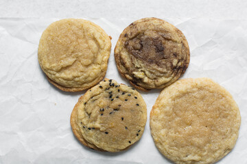 Overhead view of different types of sugar cookies, vanilla cookies, cinnamon cookie, black sesame sugar cookie on parchment paper