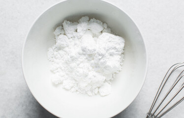 Overhead view of icing sugar in a white mixing bowl, top view of powdered sugar on a marble countertop