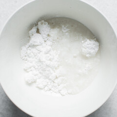 Overhead view of icing sugar mixed with water, powdered sugar dissolved in water on a white table, top view of powdered sugar glaze in a white bowl