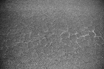 Close-up view of a cracked and weathered surface, possibly asphalt or similar material. Shows signs of age and deterioration.