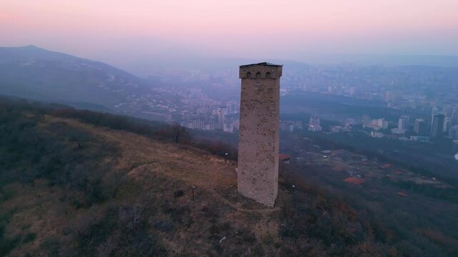 Ancient Georgian tower against the backdrop of modern Tbilisi city at dusk.
