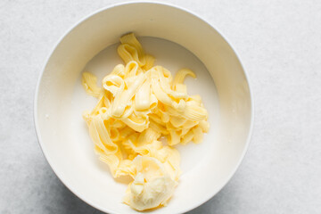 Overhead view of butter and icing sugar in a white mixing bowl, top view of butter and liquid powdered sugar on a countertop, ingredients for making buttercream, process of making russian buttercream