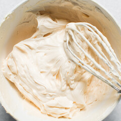 Top view of cream buttercream in a white mixing bowl, silky smooth american buttercream in a ceramic bowl, overhead view of smooth buttercream