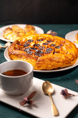 Traditional homemade banana caramel pie. French Tarte Tatin on a white plate with a cup of tea on a green, emerald background. Top view. Close-up.