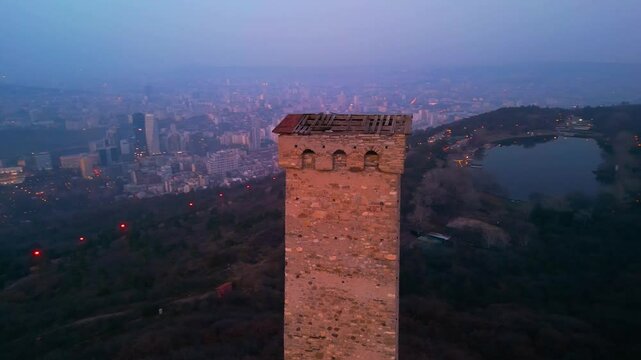 Ancient Georgian tower against the backdrop of modern Tbilisi city at dusk.