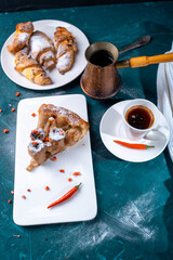 A slice of banana pie with hot chili peppers and coffee cooked in a cezve on a dark green background. French Tarte Tatin and handmade croissants on the table.