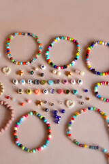 Friendship bracelet spelled with letter beads. Colorful handmade bracelets and various beads. Selective focus, pink background.