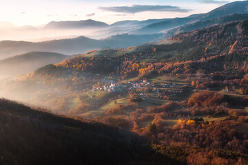  A breathtaking aerial view of an Alsatian village nestled in the mountains, with rolling hills, colorful autumn trees, and soft morning mist. A perfect scene capturing the beauty of rural France