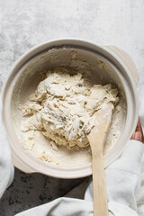 Overhead view of bread dough being mixed in a donabe, top view of homemade bread dough being mixed on granite countertop, process of making artisan bread