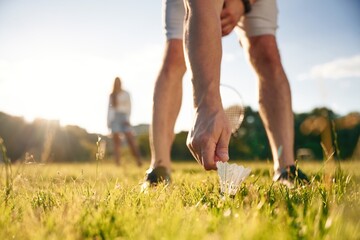 Guy is picking up the shuttlecock. Man with woman are playing badminton on the field