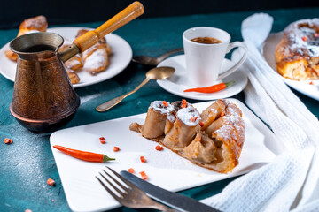 A slice of banana pie with hot chili peppers and coffee cooked in a cezve on a dark green background. French Tarte Tatin and handmade croissants on the table.