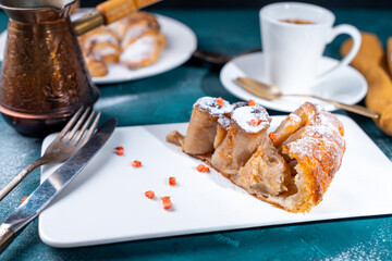 Banana dessert Tarte tatin and croissants on a dark green background with a cup of coffee brewed in a cezve and freeze-dried raspberries.